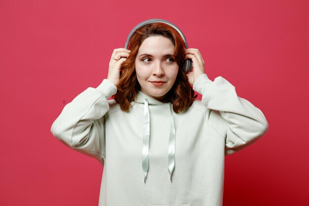 Pleased young beautiful girl in white sweater wearing headphones isolated on pink background