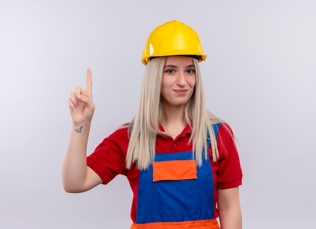 Lieta giovane ragazza bionda ingegnere costruttore in uniforme con il dito alzato su uno spazio bianco isolato