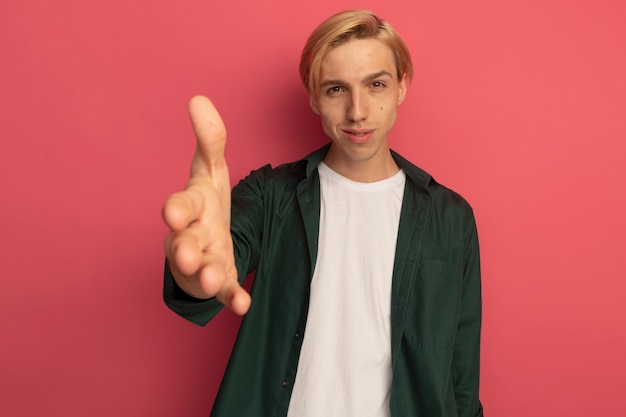 Pleased young blonde guy wearing green t-shirt holding out hand