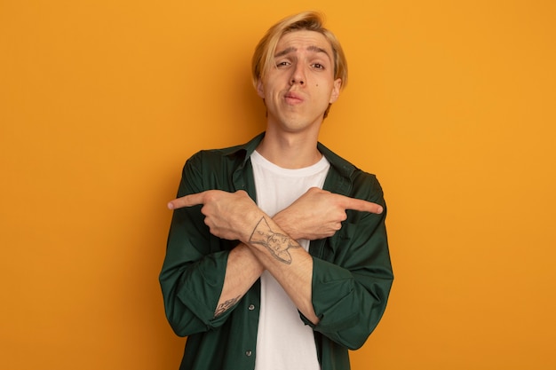 Free photo pleased young blonde guy wearing green t-shirt points at differents at sides