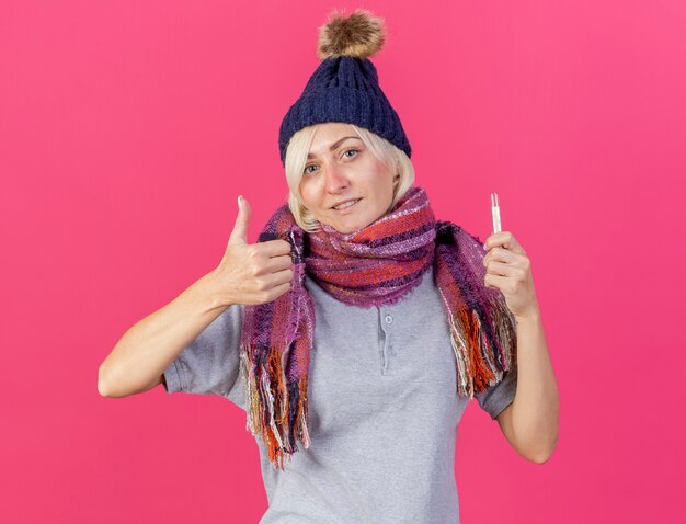 Pleased young blonde ill slavic woman wearing winter hat and scarf thumbs up