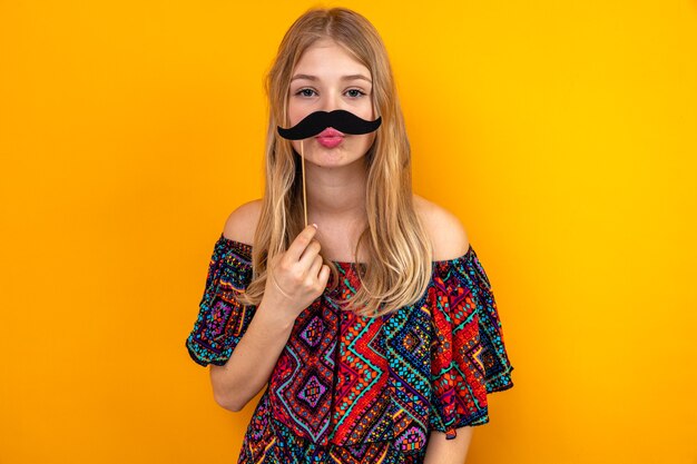 Pleased young blonde slavic girl holding fake mustache on stick 