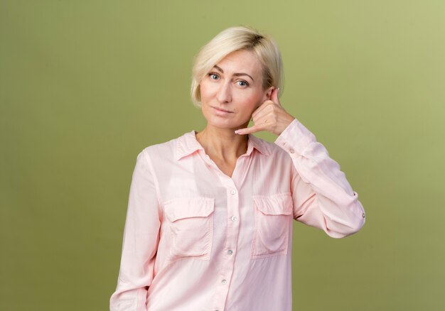 Pleased young blonde slavic woman showing phone call gesture 