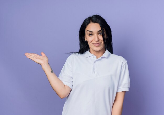 Pleased young brunette caucasian girl holds hand open isolated on purple wall