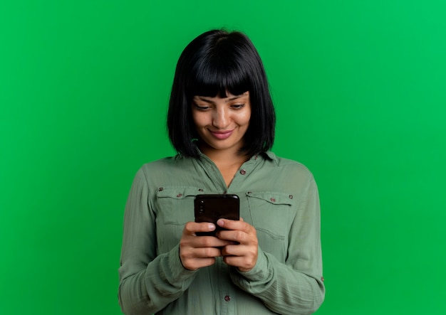 Pleased young brunette caucasian girl holds and looks at phone 