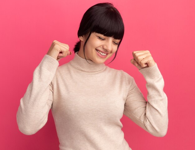Pleased young brunette caucasian girl keeps fists up