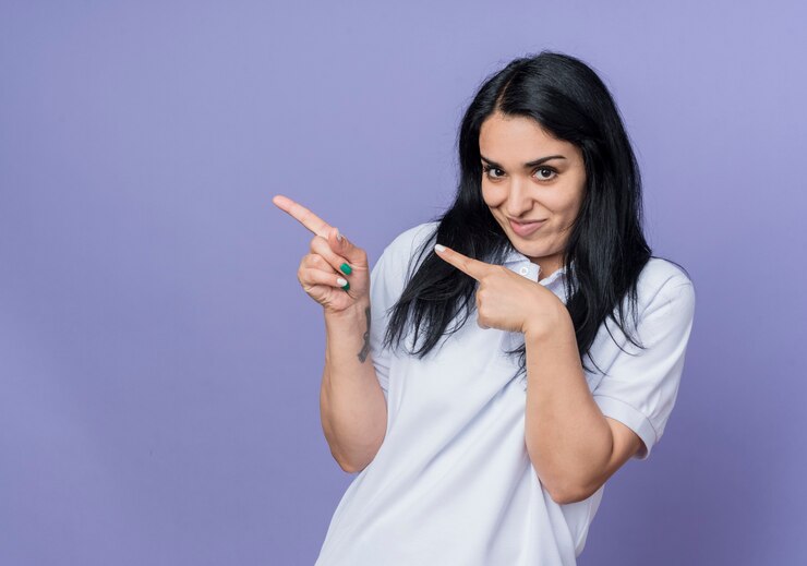 मुफ़्त फोटो pleased young brunette caucasian girl points at side looking isolated on purple wall