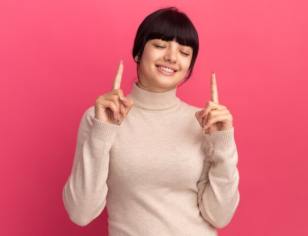 Pleased young brunette caucasian girl points up with two hands