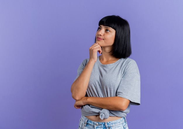 Pleased young brunette caucasian girl puts hand on chin and looks at side 