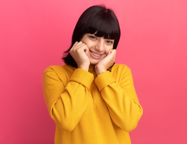 Pleased young brunette caucasian girl puts hands on face