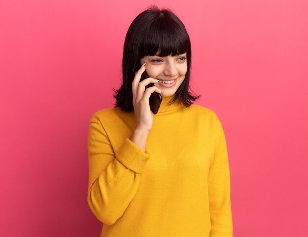 Pleased young brunette caucasian girl talks on phone looking at side on pink