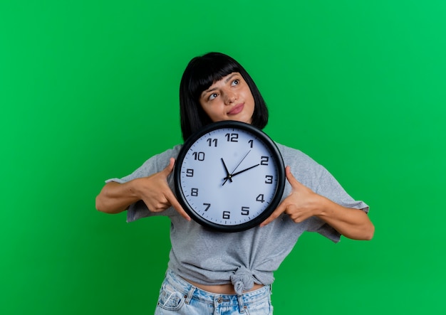 Foto gratuita la giovane donna caucasica castana soddisfatta tiene l'orologio che guarda il lato