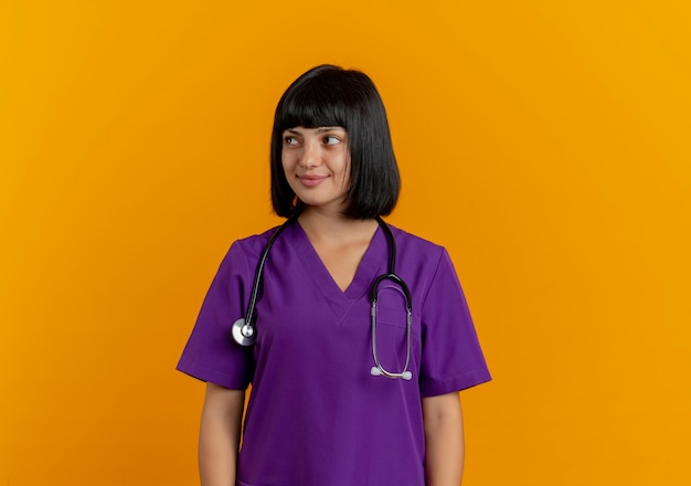 Pleased young brunette female doctor in uniform with stethoscope looks at side