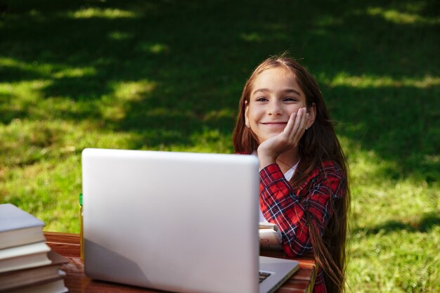 Pleased young brunette girl sitting by the table with laptop