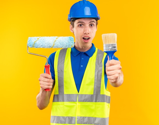 Довольный молодой человек-строитель в униформе, держащий роликовую кисть с кистью