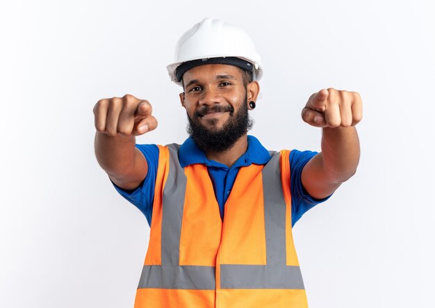 pleased young builder man in uniform with safety helmet pointing at front with two hands isolated on white wall with copy space