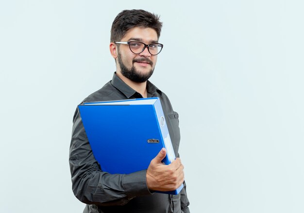 Pleased young businessman wearing glasses holding folder isolated on white background