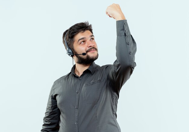 Pleased young call center man wearing headset raising and looking at fist 