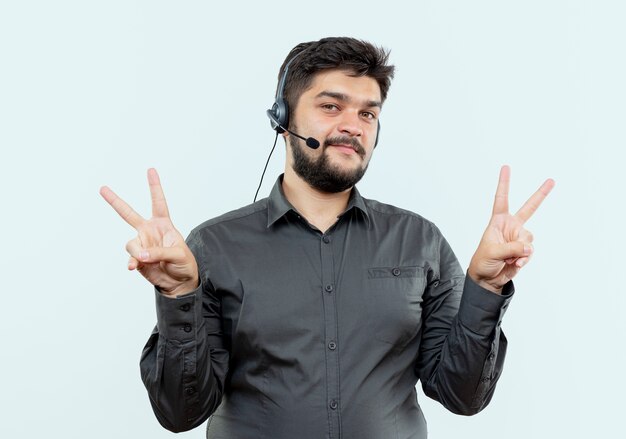 Foto gratuita felice giovane call center uomo che indossa la cuffia avricolare che mostra gesti di pace isolati su sfondo bianco