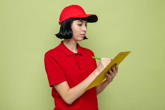 Pleased young caucasian delivery girl writing on clipboard