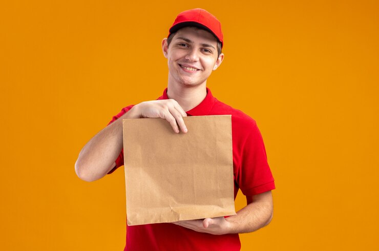 Free Photo pleased young caucasian delivery man in red shirt holding food package 