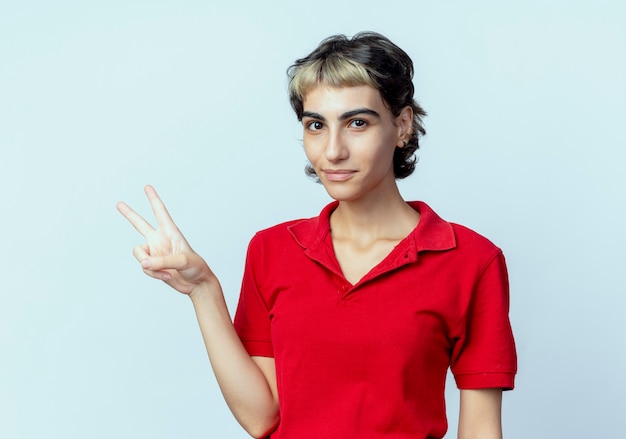 Pleased young caucasian girl with pixie haircut doing peace sign isolated on white background