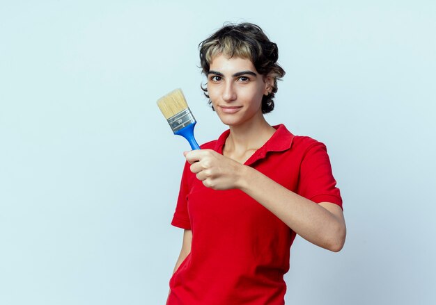 Free photo pleased young caucasian girl with pixie haircut stretching out paint brush towards camera isolated on white background with copy space