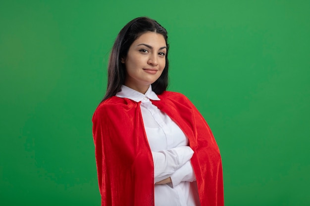 Pleased young caucasian superhero girl standing with closed posture and smiling isolated on green wall with copy space