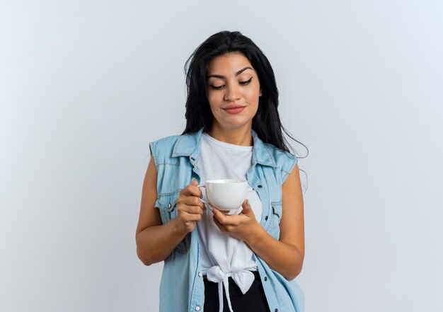 Pleased young caucasian woman holds and looks at cup