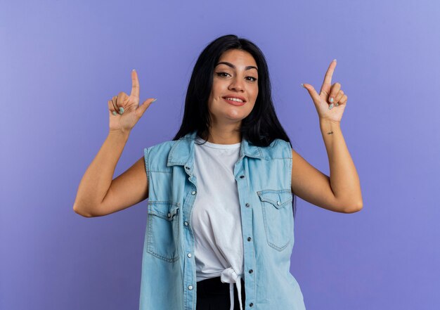 Pleased young caucasian woman points up with two hands isolated on purple background with copy space