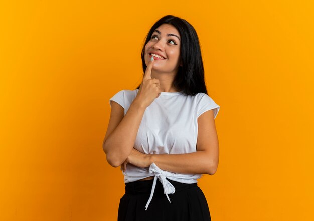 Pleased young caucasian woman puts finger on mouth looking up