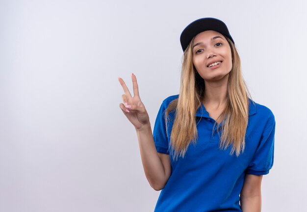 Pleased young delivery woman wearing blue uniform and cap showing peace gesture 