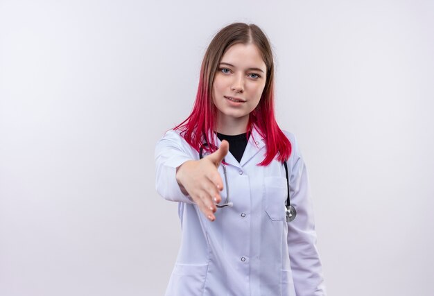 Pleased young doctor girl wearing stethoscope medical robe holding out hand to camera on isolated white background