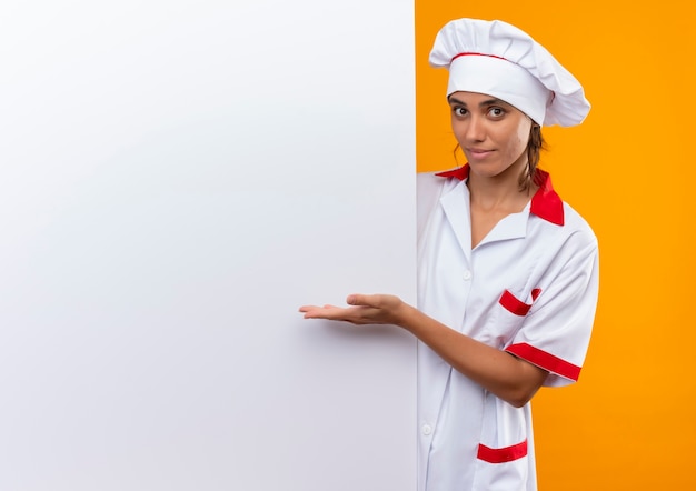 요리사 유니폼 지주 및 복사 공간이 격리 된 노란색 벽에 손 흰 벽과 포인트를 입고 기쁘게 젊은 여성 요리사