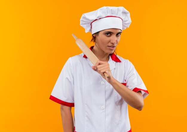 Pleased young female cook wearing chef uniform holding rolling pin around shoulder  with copy space