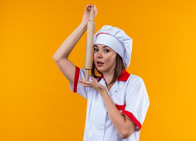 Foto gratuita piacere giovane cuoca che indossa l'uniforme dello chef tenendo il mattarello isolato sulla parete arancione orange