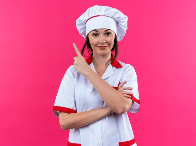 복사 공간이 있는 분홍색 벽에 격리된 측면에서 요리사 유니폼을 입은 젊은 여성 요리사를 기쁘게 생각합니다