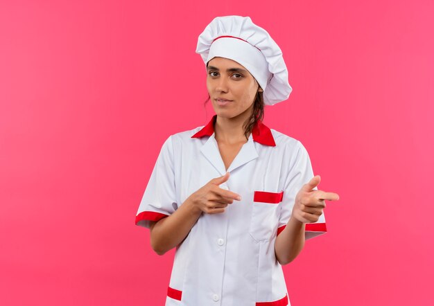 Pleased young female cook wearing chef uniform points to side with copy space