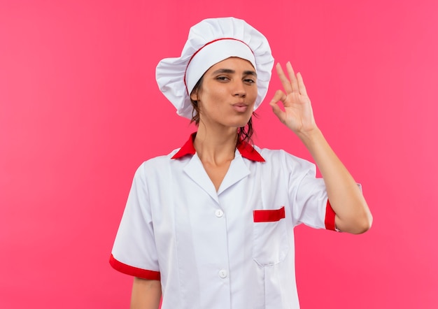 Pleased young female cook wearing chef uniform showing delicious gesture with copy space