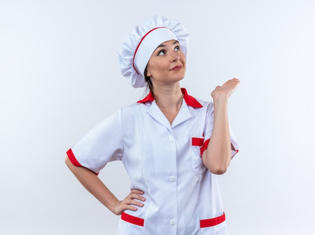 Довольная молодая женщина-повар в униформе шеф-повара, протягивая руку, изолированную на белом фоне