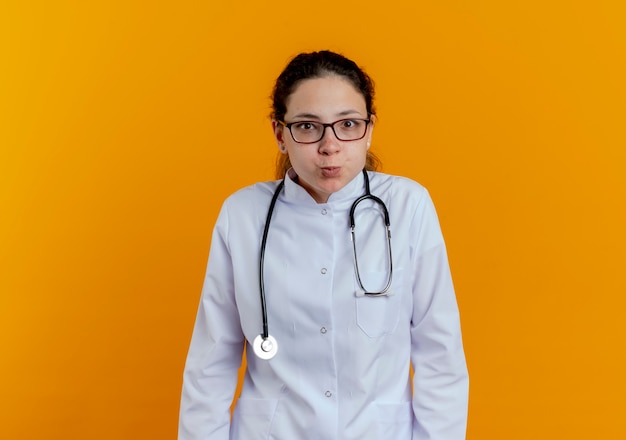 Free photo pleased young female doctor wearing medical robe and stethoscope with glasses isolated