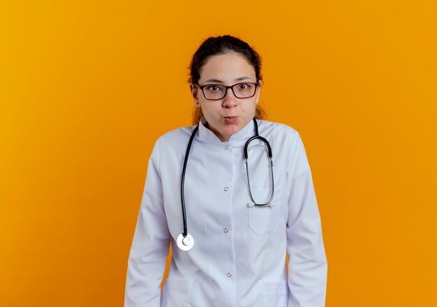 Pleased young female doctor wearing medical robe and stethoscope with glasses isolated