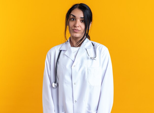 Free photo pleased young female doctor wearing medical robe with stethoscope isolated on yellow wall