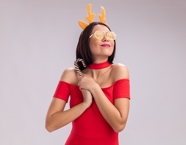 無料写真 コピースペースと白い背景で隔離の目を閉じてクリスマスクリスマスキャンディケインを保持しているトナカイの角のヘッドバンドと眼鏡を身に着けている幸せな少女