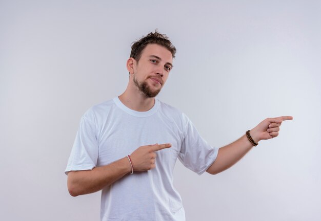 pleased young guy wearing white t-shirt points to side on isolated white background