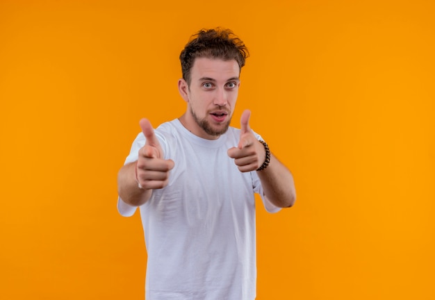 Pleased young guy wearing white t-shirt showing you gesture on isolated orange background