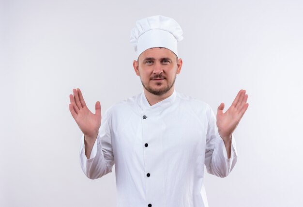 白いスペースで隔離の空の手を示すシェフの制服を着た若いハンサムな料理人を喜ばせる