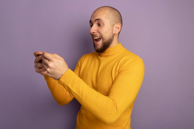 Lieto giovane bel ragazzo tenendo e guardando il telefono isolato sulla porpora