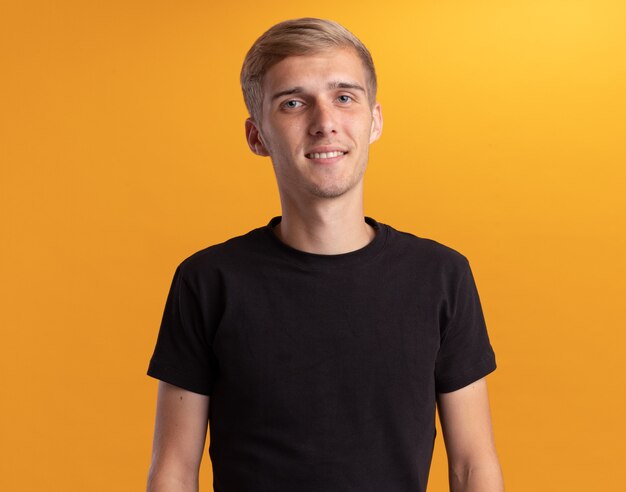 Pleased  young handsome guy wearing black shirt isolated on yellow wall