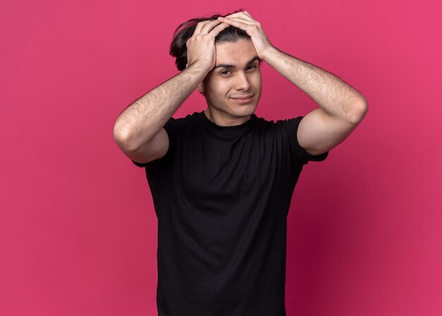 Pleased young handsome guy wearing black t-shirt grabbed head isolated on pink wall
